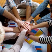 close-up-view-of-the-young-motivated-team-of-business-people-putting-hands-together-between-them-while-sitting-on-the-office-floor