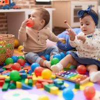 Two toddlers playing with balls and xylophone sitting on floor at kindergarten